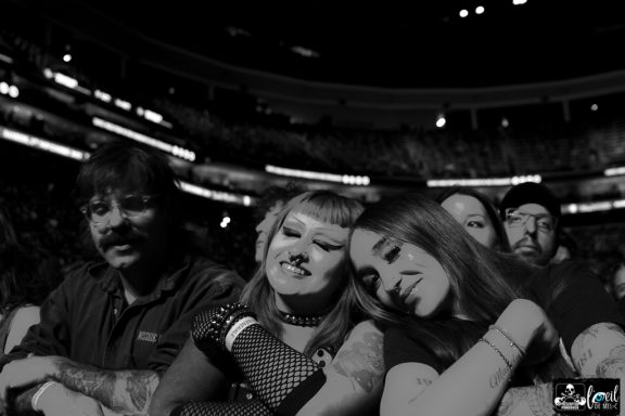 A group of fans enjoying a concert, smiling and leaning on each other.