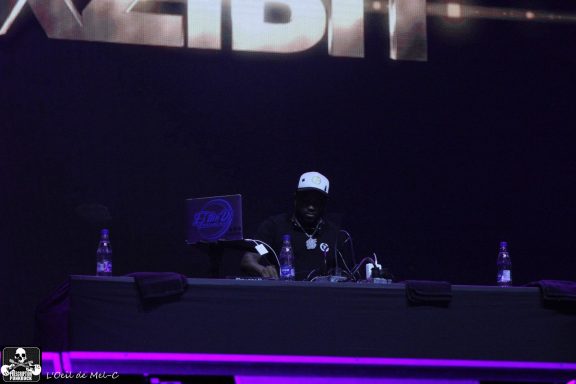 A DJ performing on stage with a dark background and purple lighting.