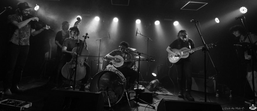 Black and white photo of a band performing on stage with various instruments.