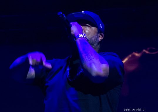 Rapper performing live on stage, gesturing with a microphone.