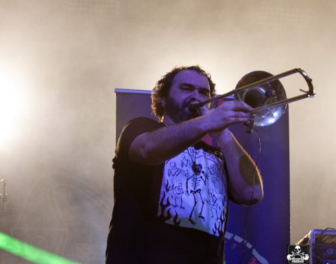 Musician performs with a trombone on stage, illuminated by colorful lights.
