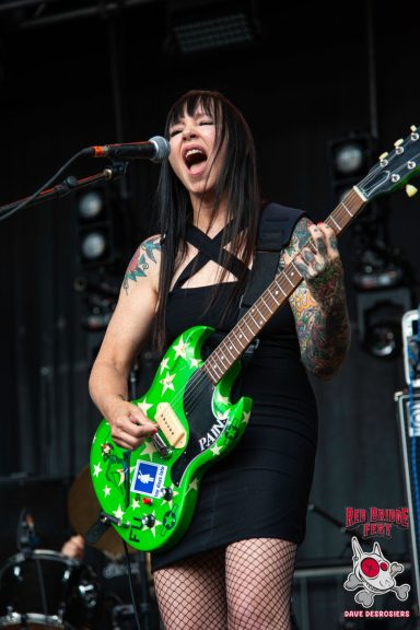 Female guitarist in a black dress, passionately performing with a green guitar.