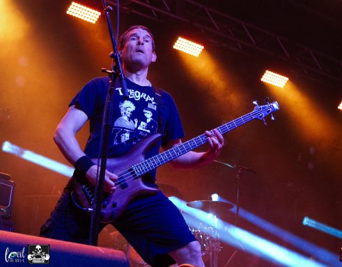 Musician playing electric guitar on stage with colorful lighting.
