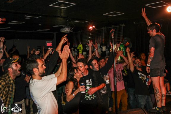 A lively crowd at a concert with a performer on stage and hands raised in excitement.