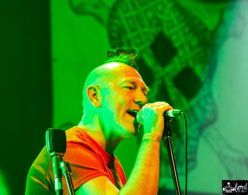 A musician singing passionately into a microphone on stage with vibrant green lighting.