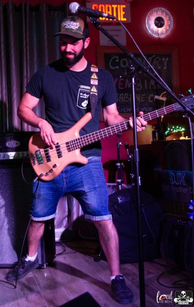 Musician playing a bass guitar on stage with a lively atmosphere.