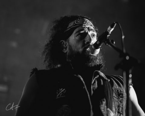 Musician singing into a microphone, wearing a bandana and dark clothing.