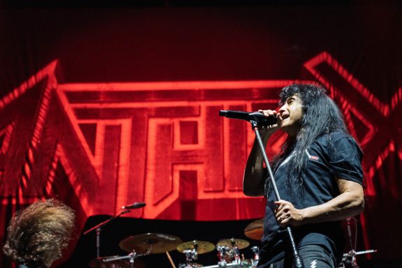 Lead vocalist performing on stage with a vibrant red logo backdrop.