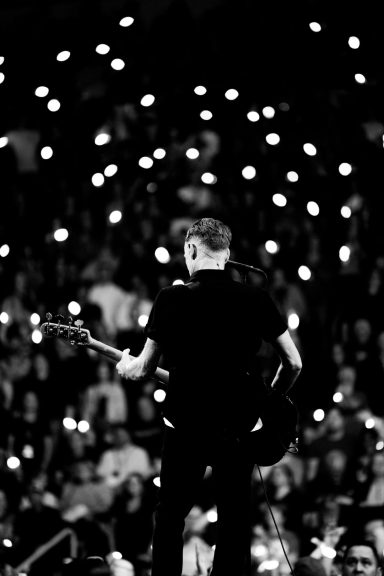 Bryan Adams - Canada Musician performing on stage, illuminated by audience's lights in a dark setting.