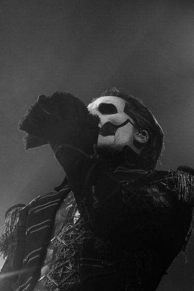 A performer with a skull face paint singing on stage under dim lighting.