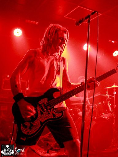 Musician playing electric guitar under red stage lights.