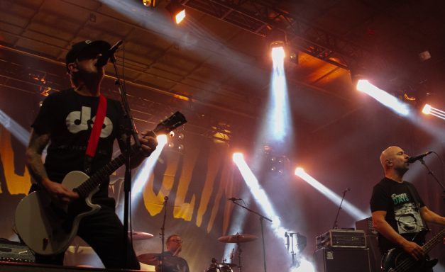 Two musicians performing on stage with bright lighting and energetic atmosphere.
