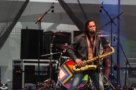 Musician playing saxophone on stage with colorful drum kit and microphones.