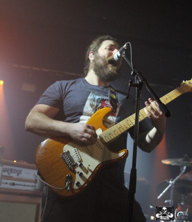Musician with a beard passionately performing and playing an electric guitar on stage.