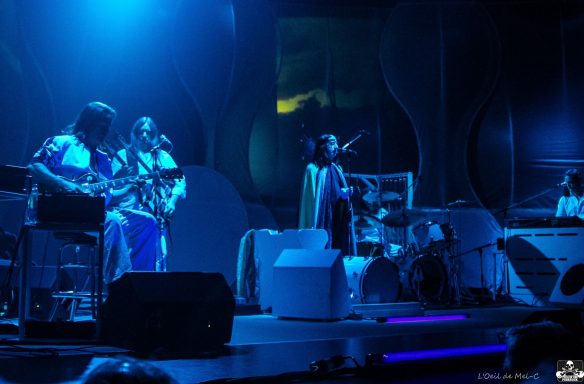 A band performing on stage with instruments and a dramatic blue lighting backdrop.