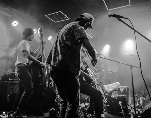 Band performing on stage with instruments, illuminated by stage lights.
