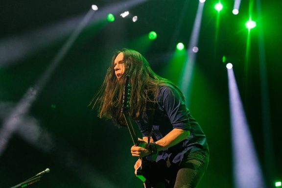 Musician performing passionately on stage with green lights in the background.