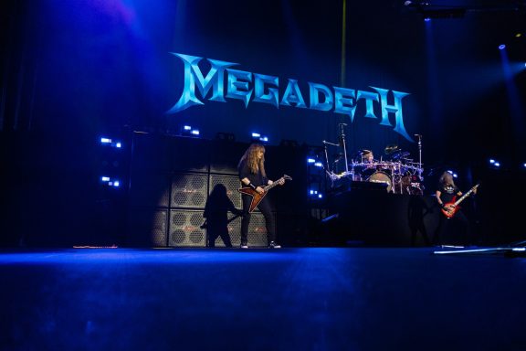 Megadeth performing live on stage with dramatic lighting and band members in action.