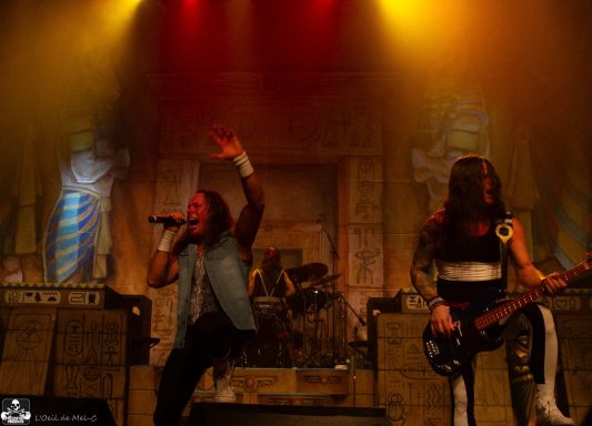 Two musicians perform on stage with dramatic lighting and a backdrop of statues.