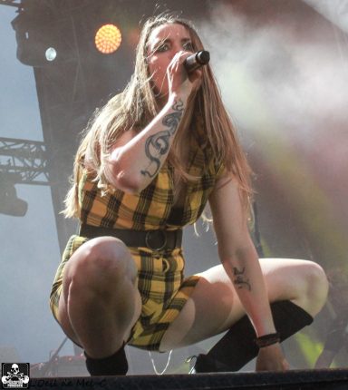 Person in a yellow plaid dress singing into a microphone on stage.