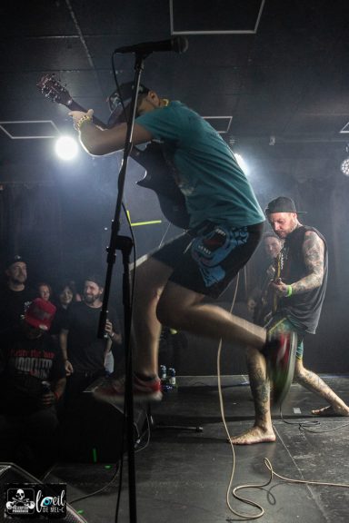 Straightline - L'Anti-Bar & Spectacles Musicians performing on stage, with one guitarist mid-jump and a crowd in the background.