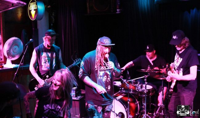 Band performing on stage with instruments, energetic atmosphere and colorful lighting.