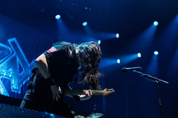 Guitarist performing on stage with intense lighting and motion.