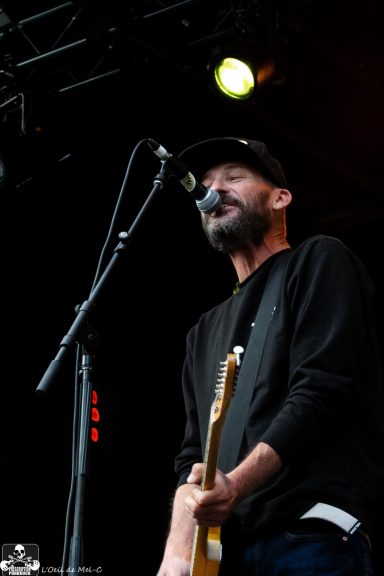 Man singing passionately into a microphone while playing guitar on stage.