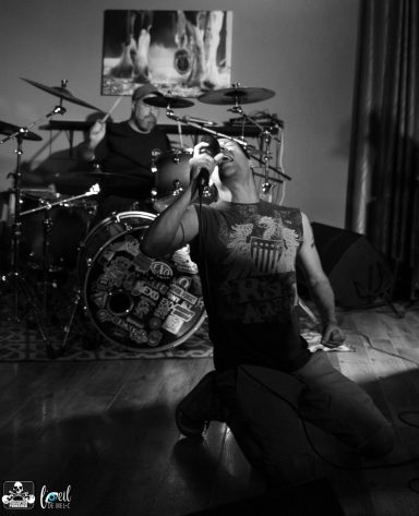 A musician performs passionately on stage while a drummer plays in the background.