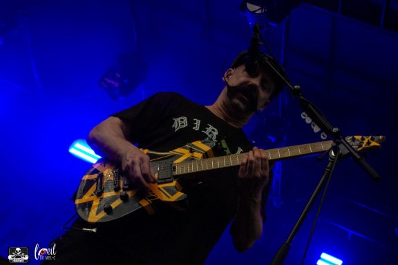 Musician playing a guitar on stage under blue lights.