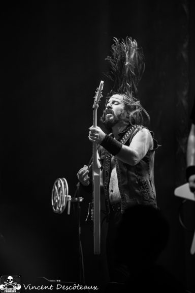 Musician performing on stage, playing guitar with long hair in motion.