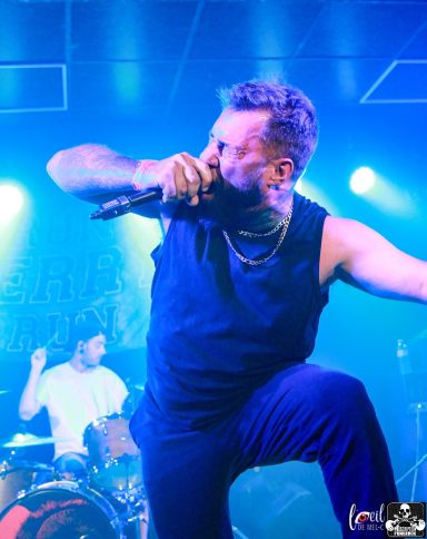 Singer performing passionately on stage with a drummer in the background.