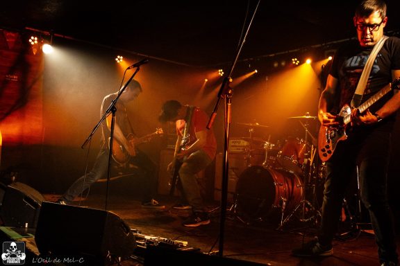 A band performs energetically on stage with dramatic lighting.