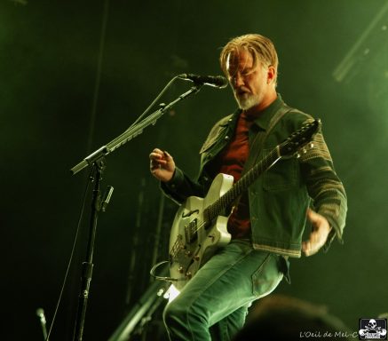 Musician performing on stage with a guitar and microphone, illuminated by green lights.