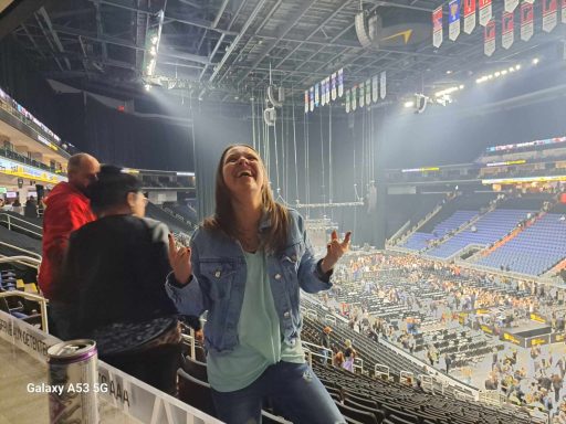 A woman joyfully celebrating at a concert venue, with fans in the background.