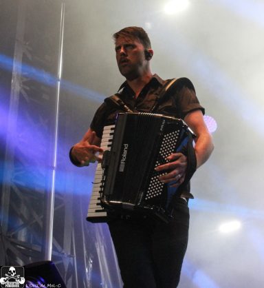 Musician playing an accordion on stage with dramatic lighting in the background.
