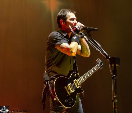 Musician performing on stage with a guitar, microphone, and dramatic lighting.