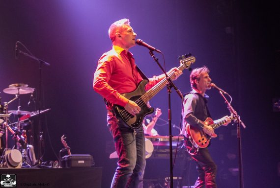 Two musicians perform on stage; one sings while the other plays guitar.