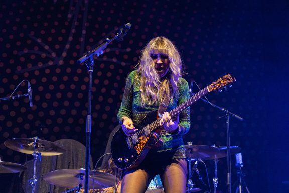 The Damn Truth - Centre Videotron Female guitarist performing on stage with a focused expression, surrounded by musical instruments.