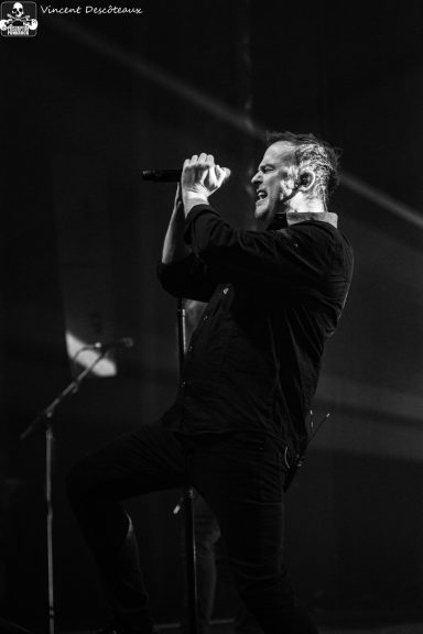 A musician performs passionately on stage, holding a microphone in a dramatic pose.