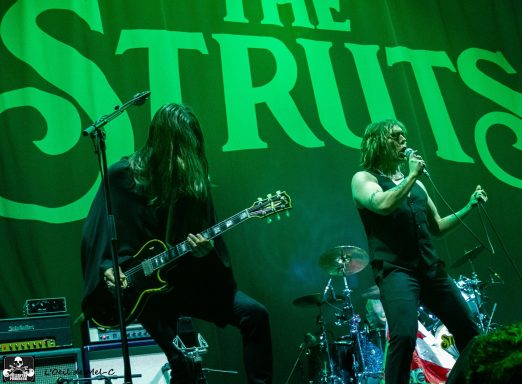 A rock band performing on stage with dramatic lighting and instruments visible.