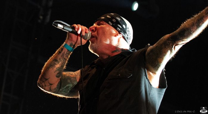 Male singer with tattoos performing passionately on stage, wearing a bandana and black outfit.