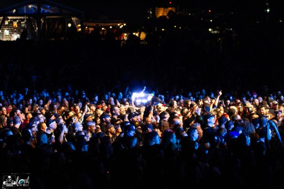 Crowd of enthusiastic concertgoers with raised hands under bright lights.