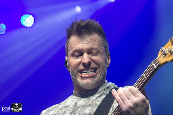 Smiling guitarist performing on stage with colorful lighting.