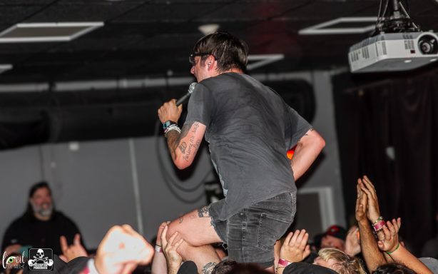 A performer singing energetically on stage, supported by fans below.