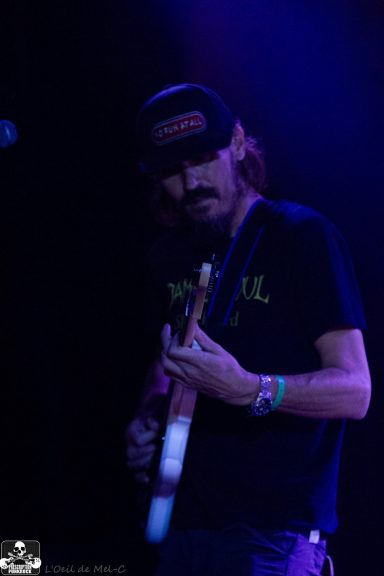 A musician playing guitar on stage, wearing a black cap and t-shirt.
