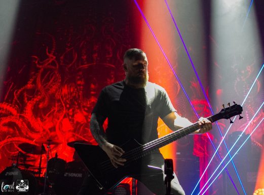 A musician plays an electric guitar on stage with vibrant lighting in the background.
