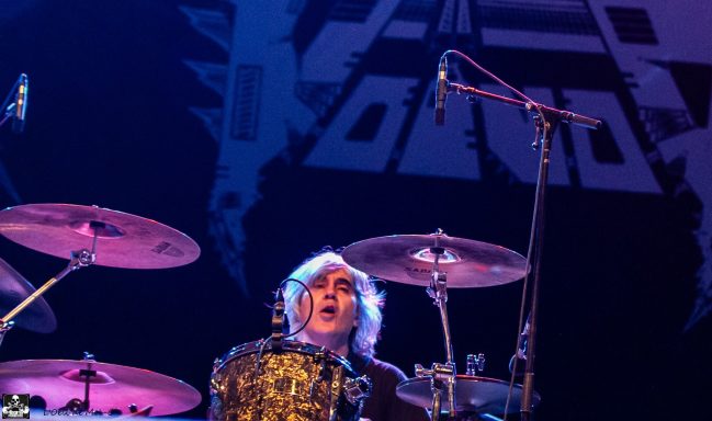 Drummer playing on stage with a dynamic expression and visible drum kit.