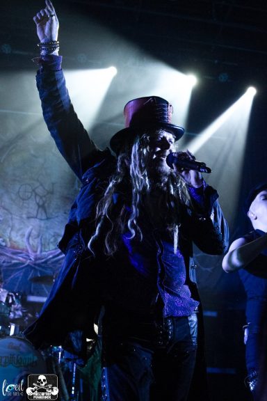 A musician in a black hat performs energetically on stage with dramatic lighting.