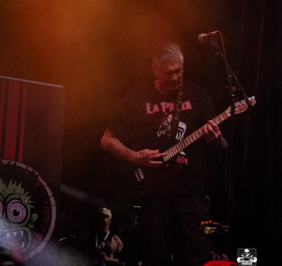 A musician playing guitar on stage with smoke and colorful lighting in the background.